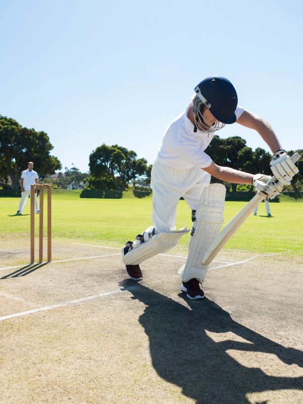 Young man playing cricket at field against clear sky on sunny day
